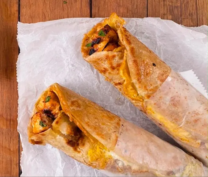 Two chicken katti rolls in flaky paratha with a bowl of green chutney