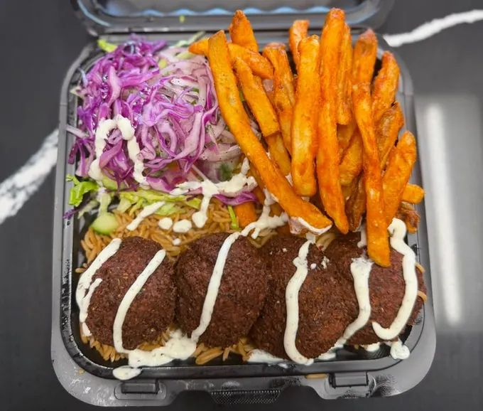 Falafel platter with crispy falafel over seasoned rice, red cabbage slaw, seasoned fries and white sauce