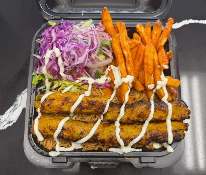 Seekh kebab platter with grilled kebab skewers over seasoned rice, slaw, seasoned fries and white sauce